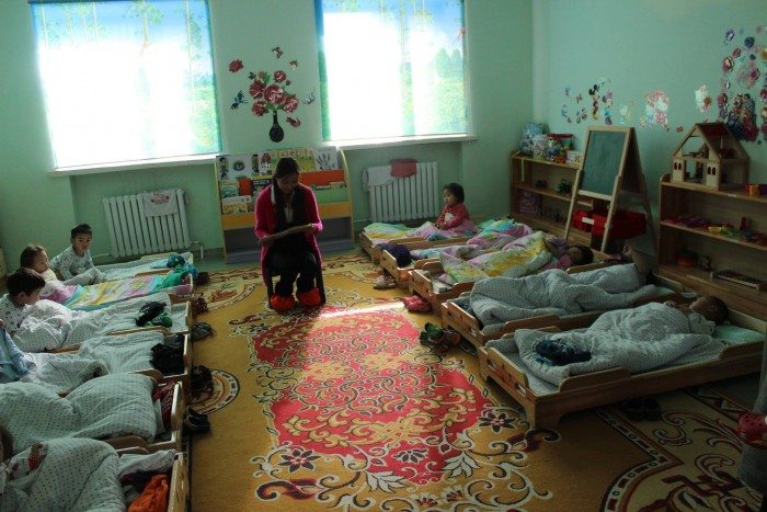 Local university student volunteer reads to kindergarten students before naptime in Mongolia.