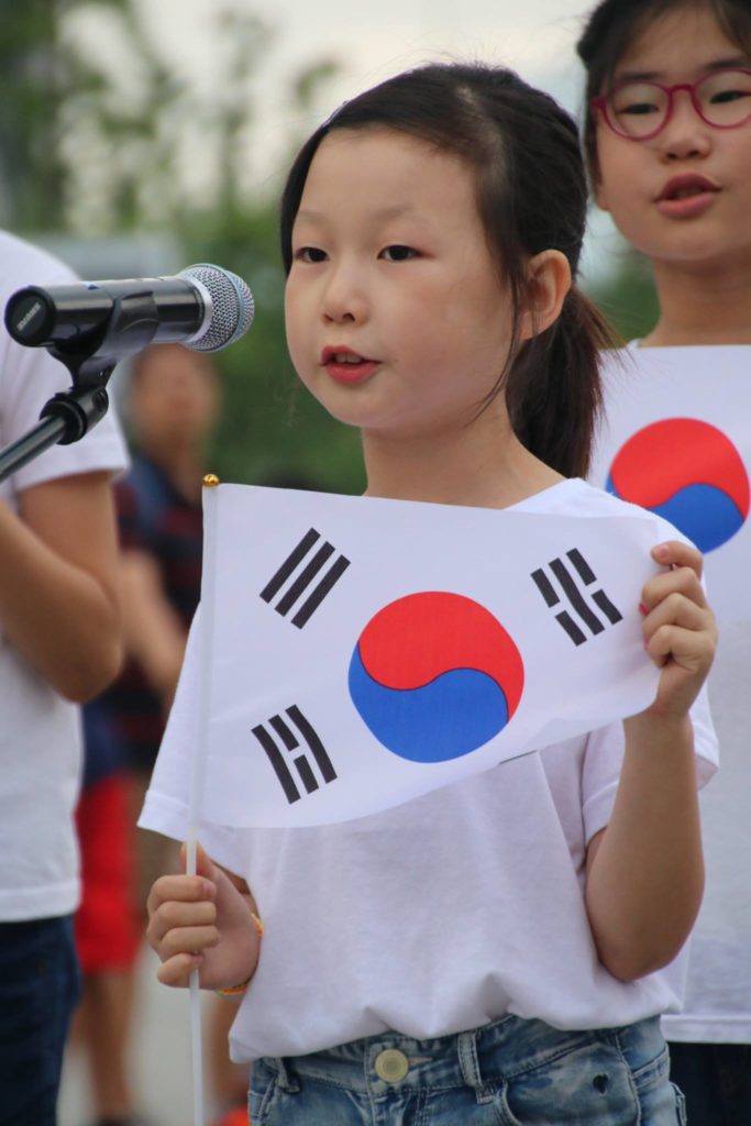 Young girl in children's choir sings “Arirang” ,holding up the taegeukki, symbolism for both North and South Korea.